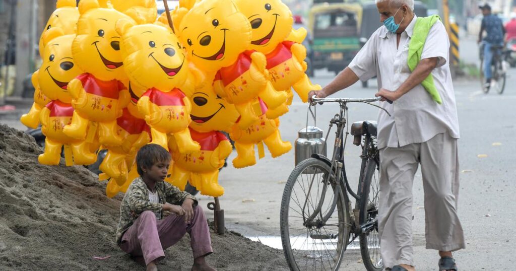 cyclist walking nearby a boy sitting and selling cartoon balloons